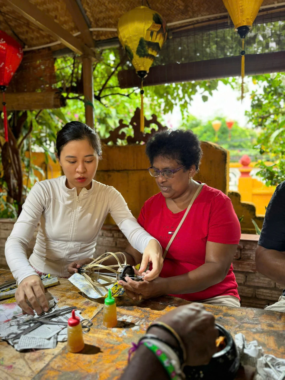 An instructor guiding a participant as she works on a small lantern frame.
