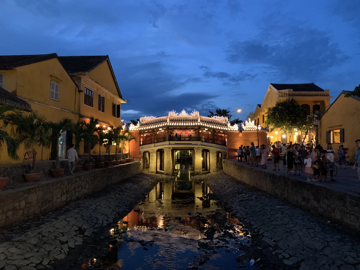 The restored Japanese Covered Bridge glows at blue hour between yellow historic buildings in Hoi An.
