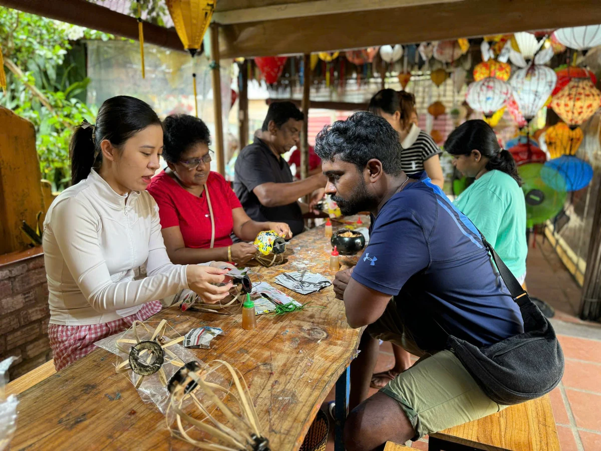 Participants and an instructor working with lantern frames and fabric at a wooden workshop table.