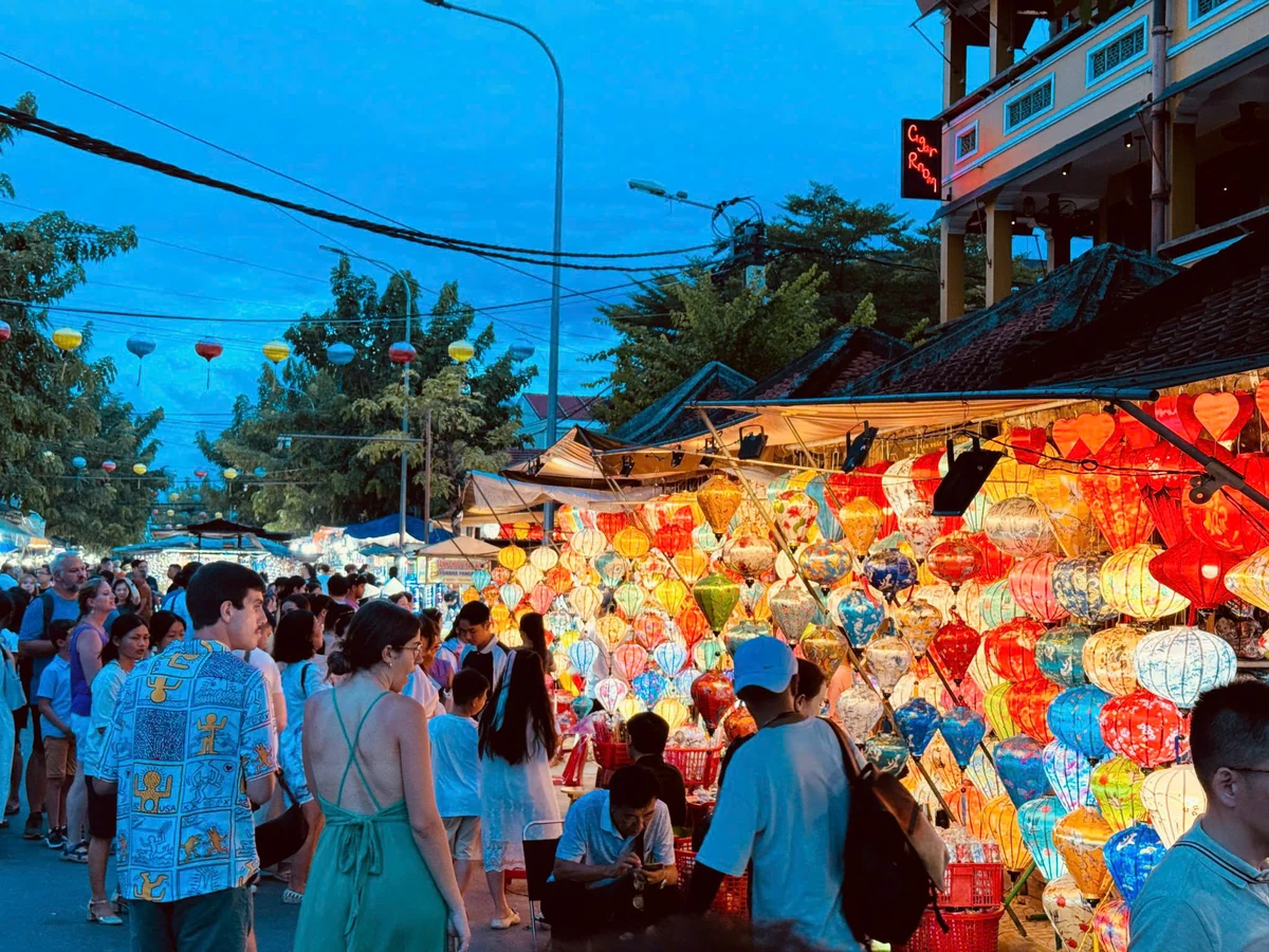 Visitors browse brightly lit lantern stalls at the Hoi An night market in the early evening.