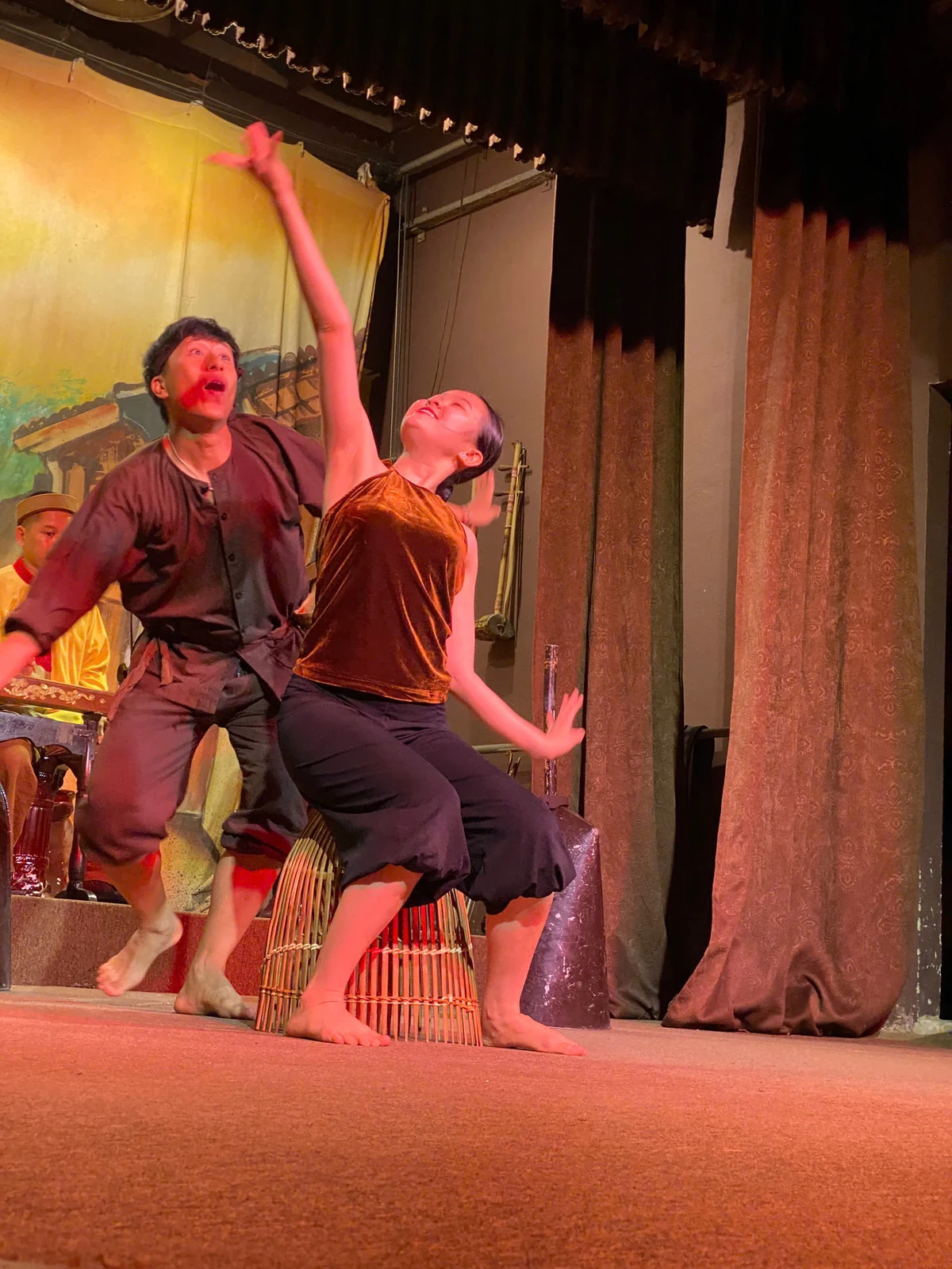Two dancers perform with bamboo fishing-basket props on a small indoor stage in Hoi An.