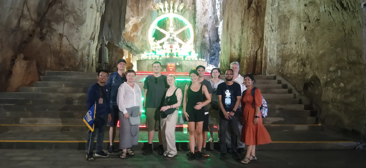 A travel group beside an illuminated Buddhist shrine and stone steps inside Am Phu Cave at the Marble Mountains.