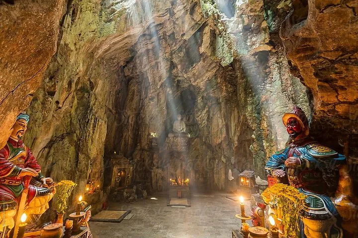 Sunbeams falling through the roof of Huyen Khong Cave onto the cavern floor and Buddhist shrines.