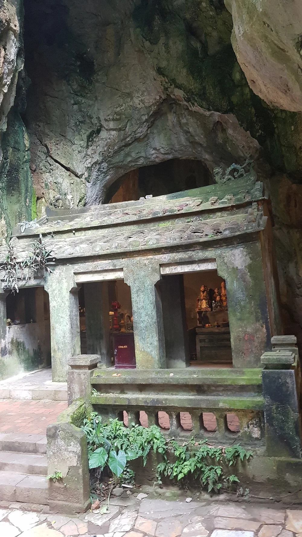 A weathered three-door Buddhist shrine beneath the rock walls of Tang Chon Cave in the Marble Mountains.