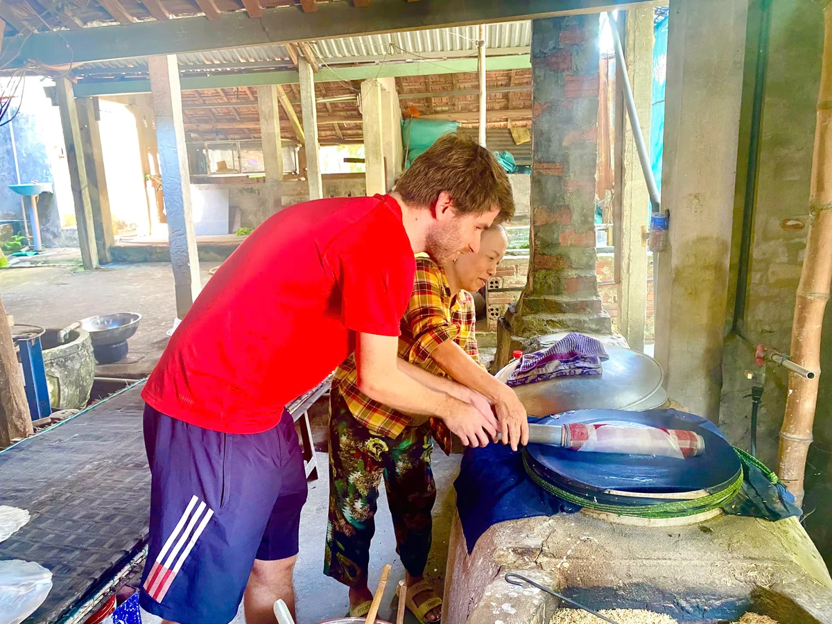 A visitor and local host work together at a traditional rice-paper steaming station.